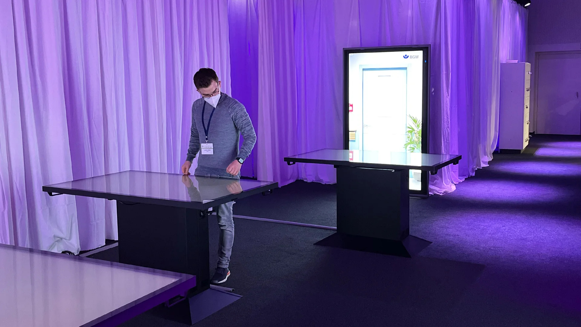 Mitarbeiter bedient einen Multitouch-Tisch im violett beleuchteten Messestand