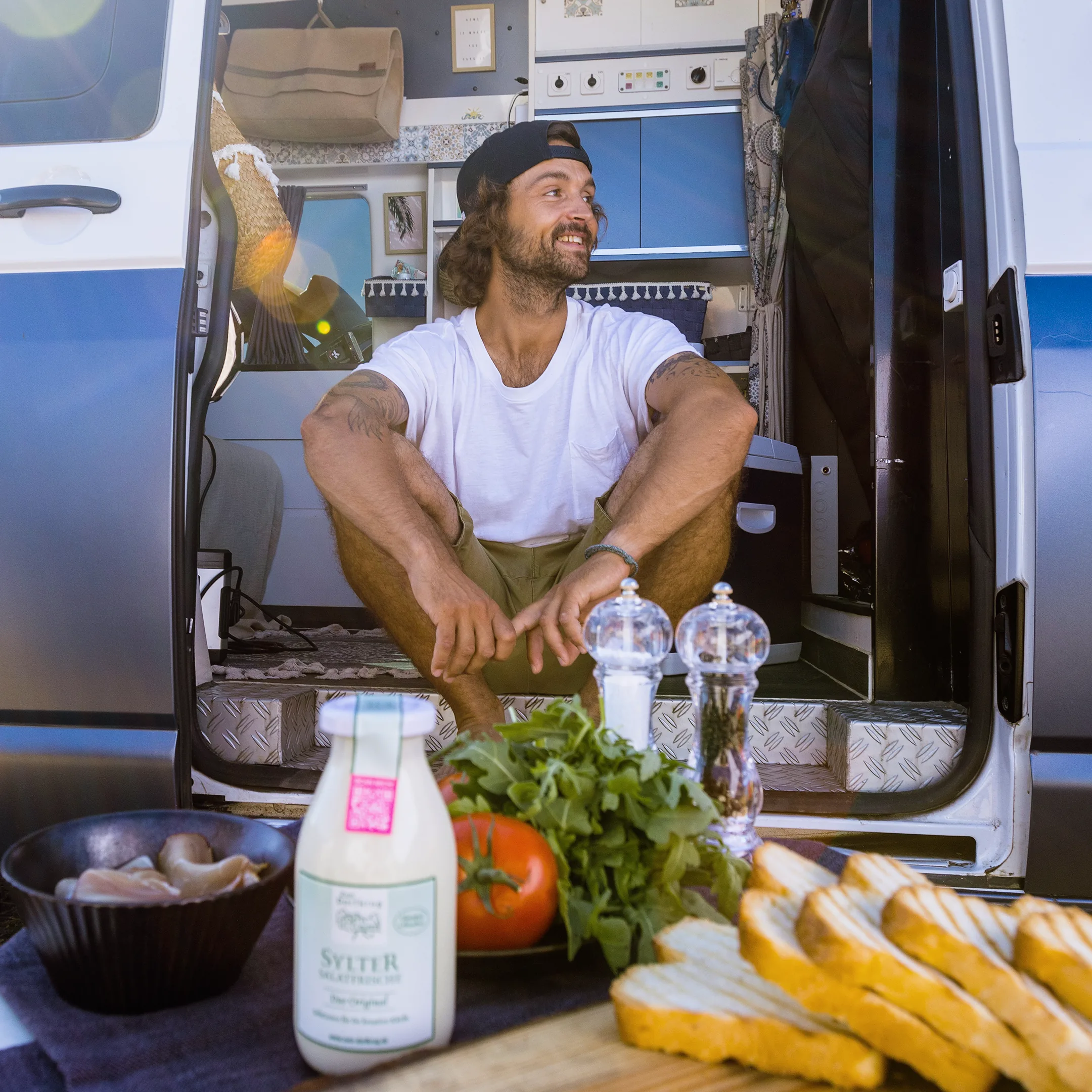 Mann vor einem Campervan, davor Zutaten und eine Flasche Sylter Salatfrische